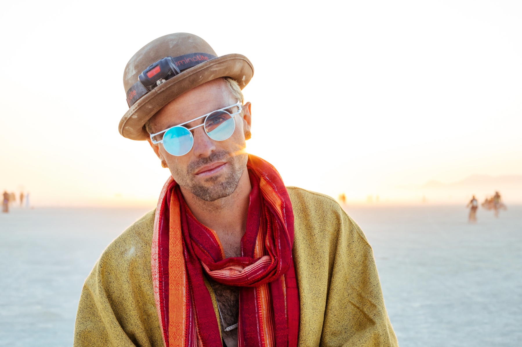 Galen Oakes on the playa at Burning Man, wearing a dust-covered hat, mirrored glasses and a red scarf.